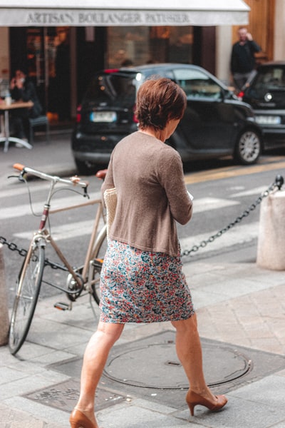 穿着棕色长袖衬衫和蓝白花裙子的女人站在人行道上
